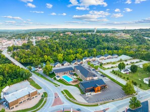 An aerial view of a town with a prominent building with a blue roof, a swimming pool, and a large parking lot. - Rc305a- The Landing Pad 2 Bedroom Condo (Branson)