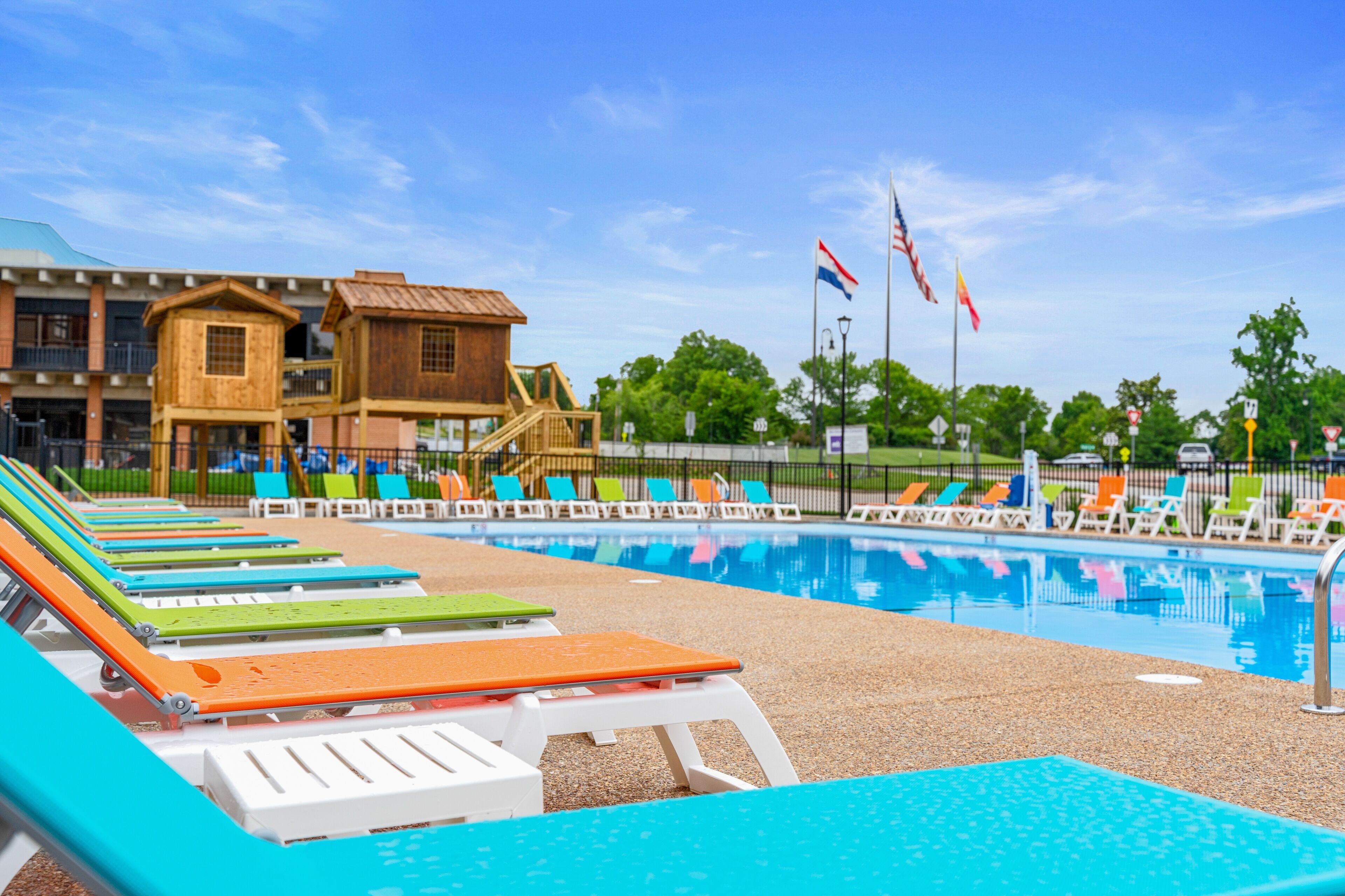A swimming pool with lounge chairs, a wooden building, and flags.