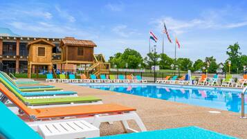 A swimming pool with lounge chairs, a wooden building, and flags.