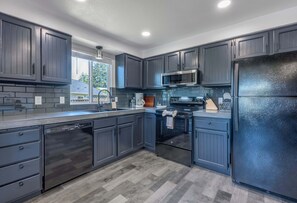 A modern kitchen with dark cabinetry, stainless steel appliances, and a herringbone-patterned floor.