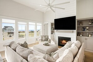 Ein geräumiges Wohnzimmer mit Kamin, großen Fenstern und Deckenventilator.