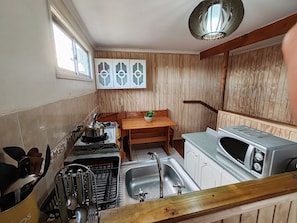 A compact kitchen with a stove, sink, and a microwave. There is a wooden table with a plant, and a window with decorative glass panels.
