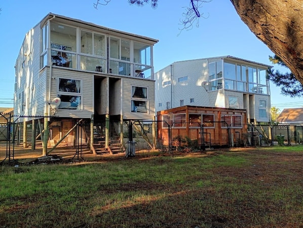 Two multi-story buildings with balconies, a fenced yard, and a tree.