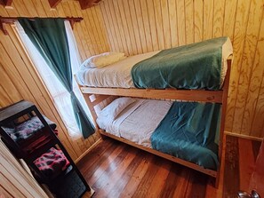Ein Etagenbett mit zwei Schlafstellen, Holzwänden, einem kleinen Tisch mit Stuhl und einem Fenster mit Vorhängen.