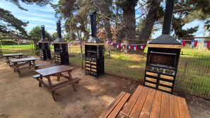 Außenliegende Grillstationen, Picknicktische und ein eingezäunter Bereich mit Bäumen.