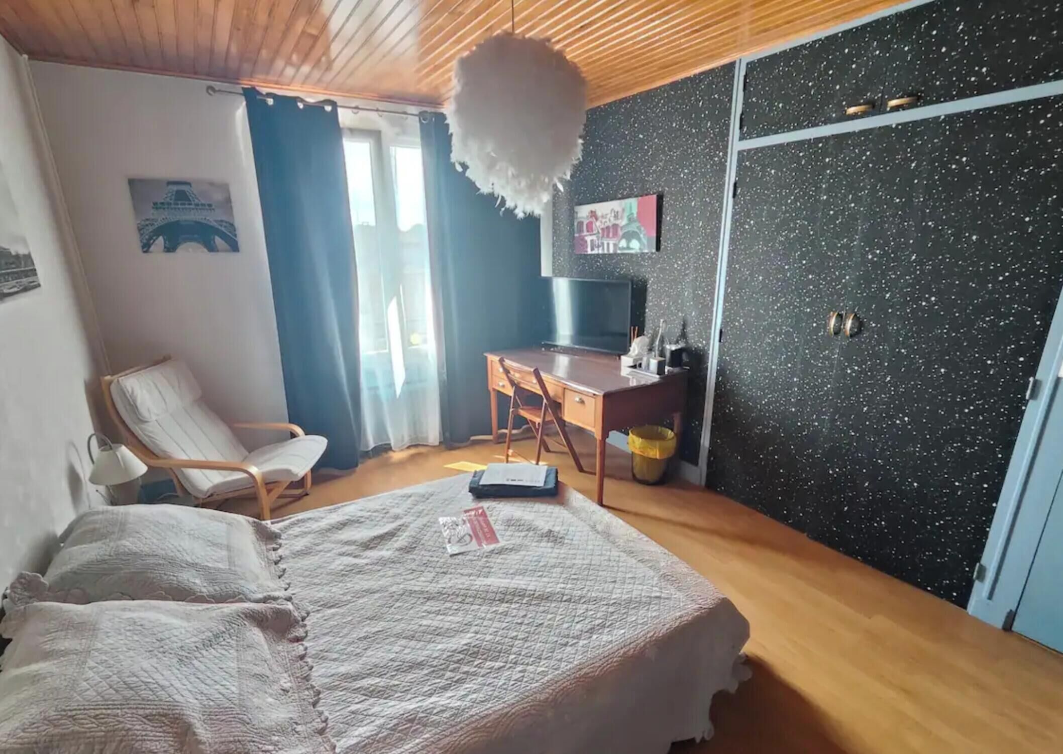 Een slaapkamer met een bed, een stoel, een bureau, een televisie en een muur met een schilderij.