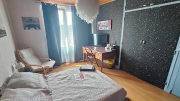 Een slaapkamer met een bed, een stoel, een bureau, een televisie en een muur met een schilderij.
