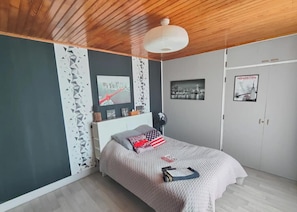Une chambre à coucher avec un lit, un t éléviseur fixé au mur, une affiche et une armoire.