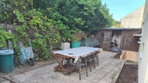 A patio with a table and chairs, a wheelbarrow, a green trash bin, and a shed in the background. - Bed and breakfast in the center of Migennes, near train station and amenities (Migennes)