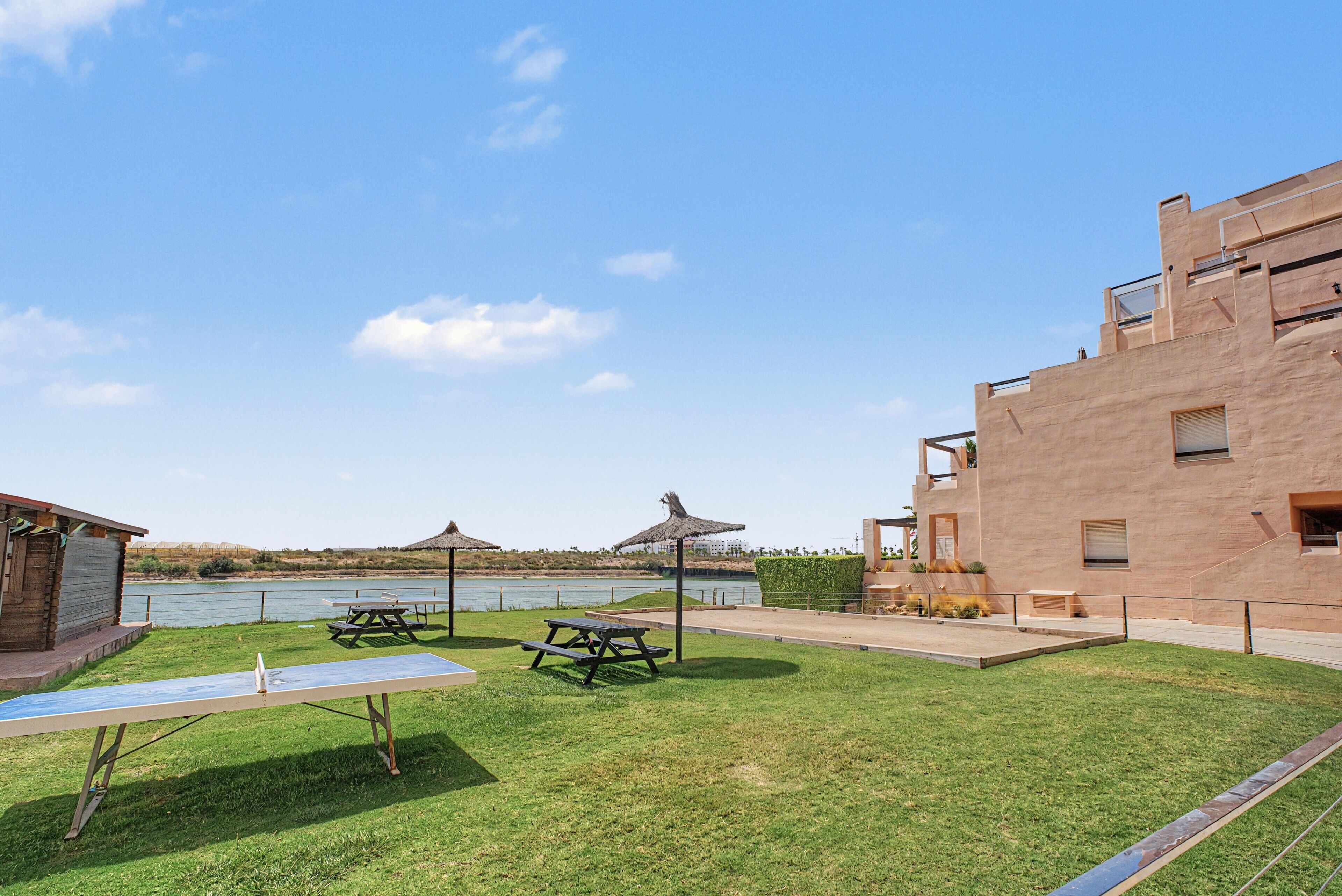 A grassy outdoor area with picnic tables and a building with a flat roof.