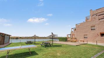 A grassy outdoor area with picnic tables and a building with a flat roof.