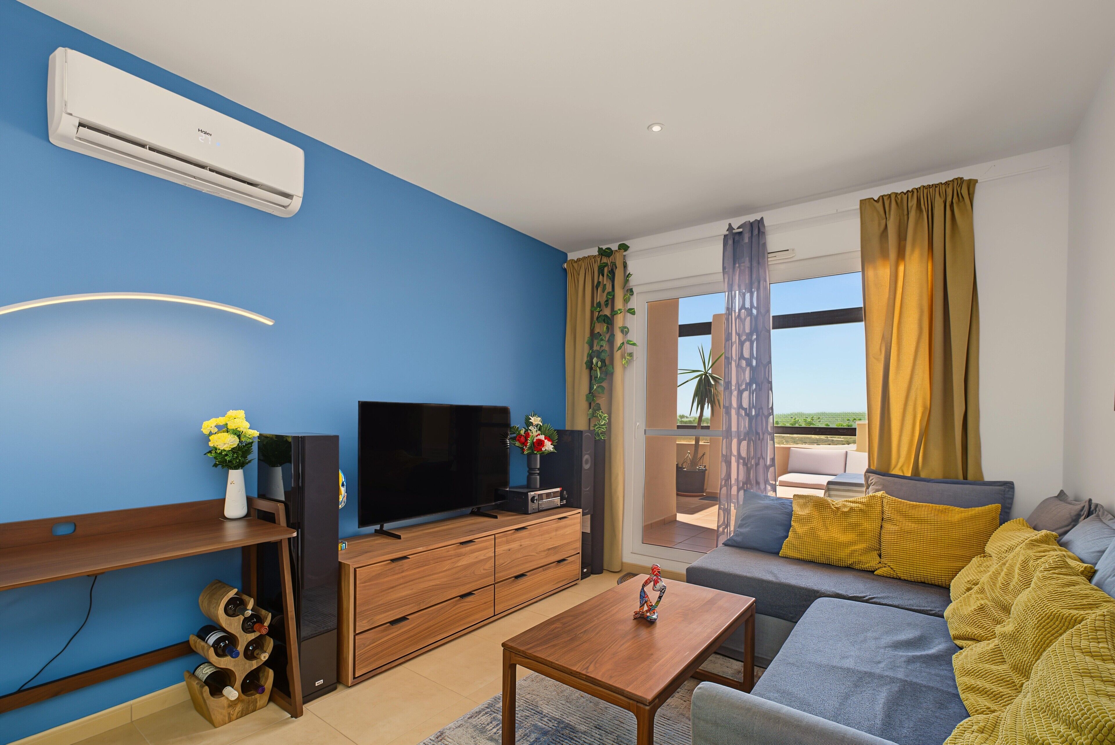 Ein modernes Wohnzimmer mit Flachbildfernseher, Holzmöbeln, einem Couchtisch und Blick ins Freie.