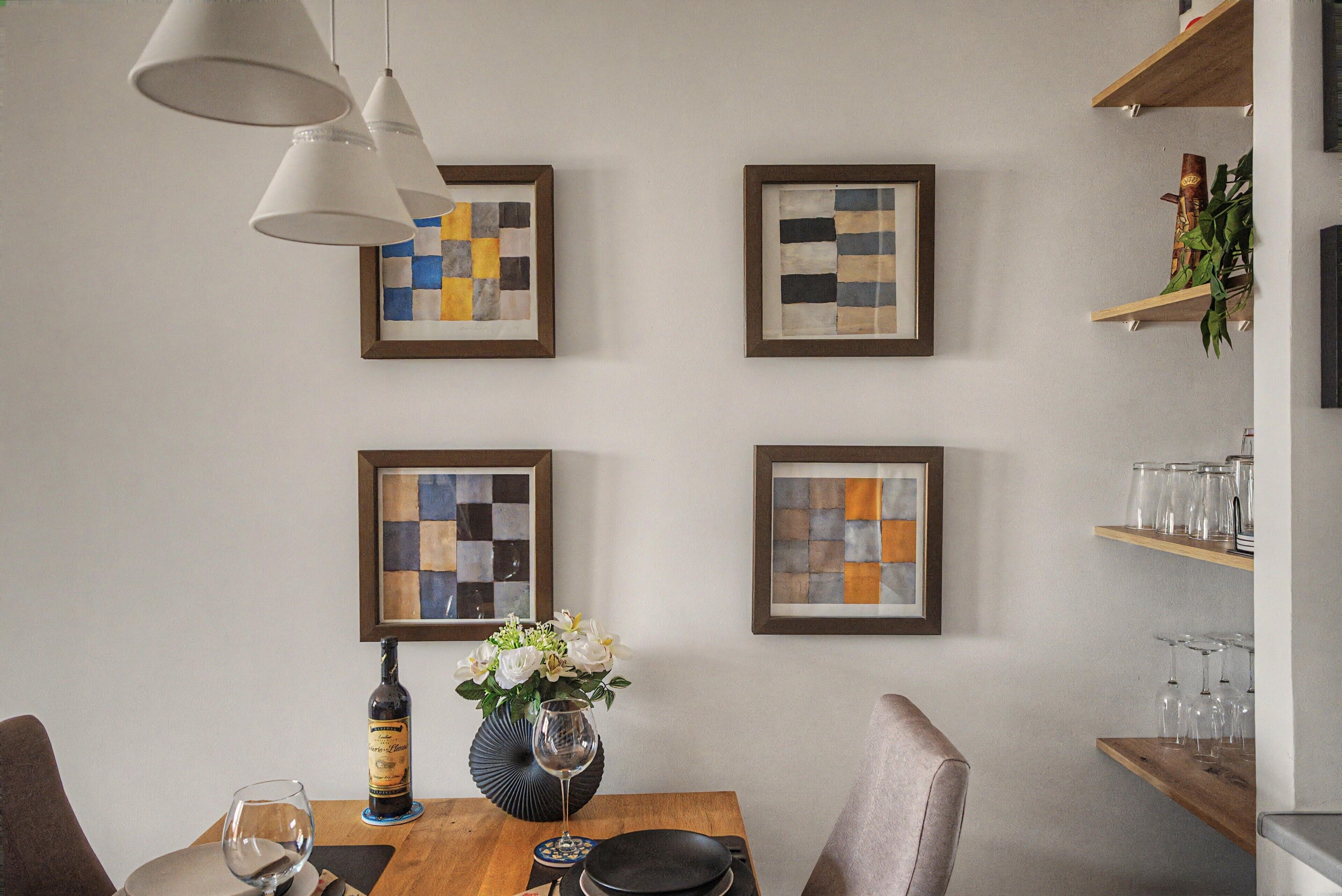 A dining area with a wooden table, chairs, a vase with flowers, and framed artwork on the wall.