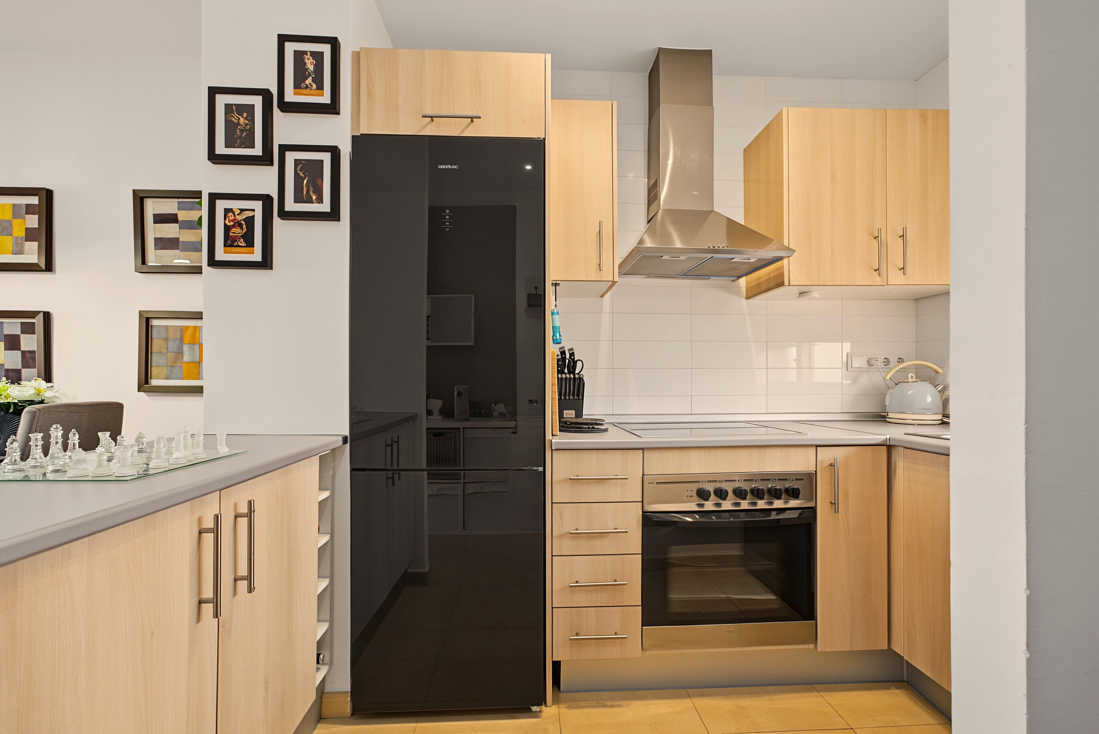 A modern kitchen with wooden cabinets, a black refrigerator, a stainless steel range hood, and a built-in oven.