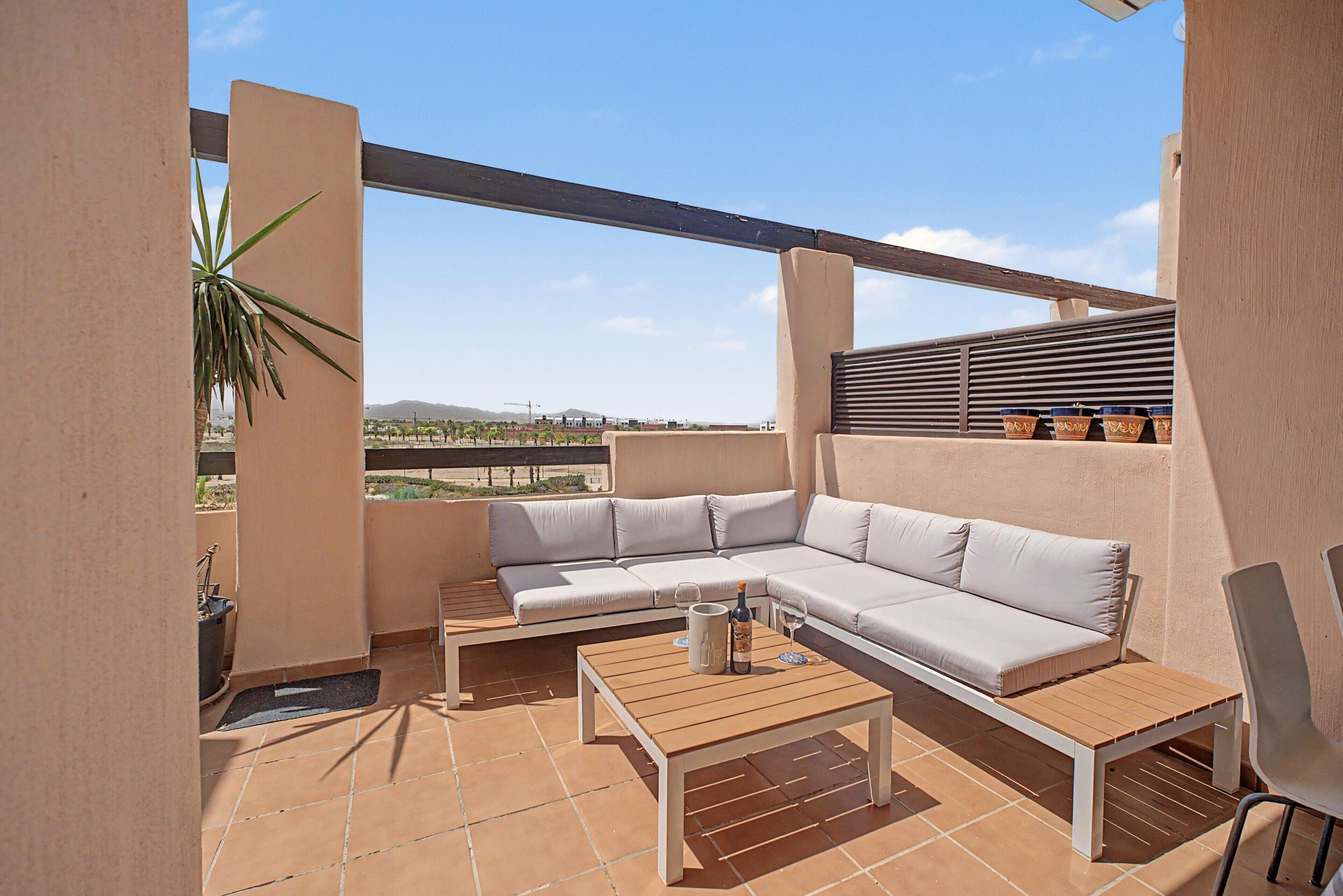 A rooftop terrace with a beige sectional sofa, a wooden table, and potted plants.