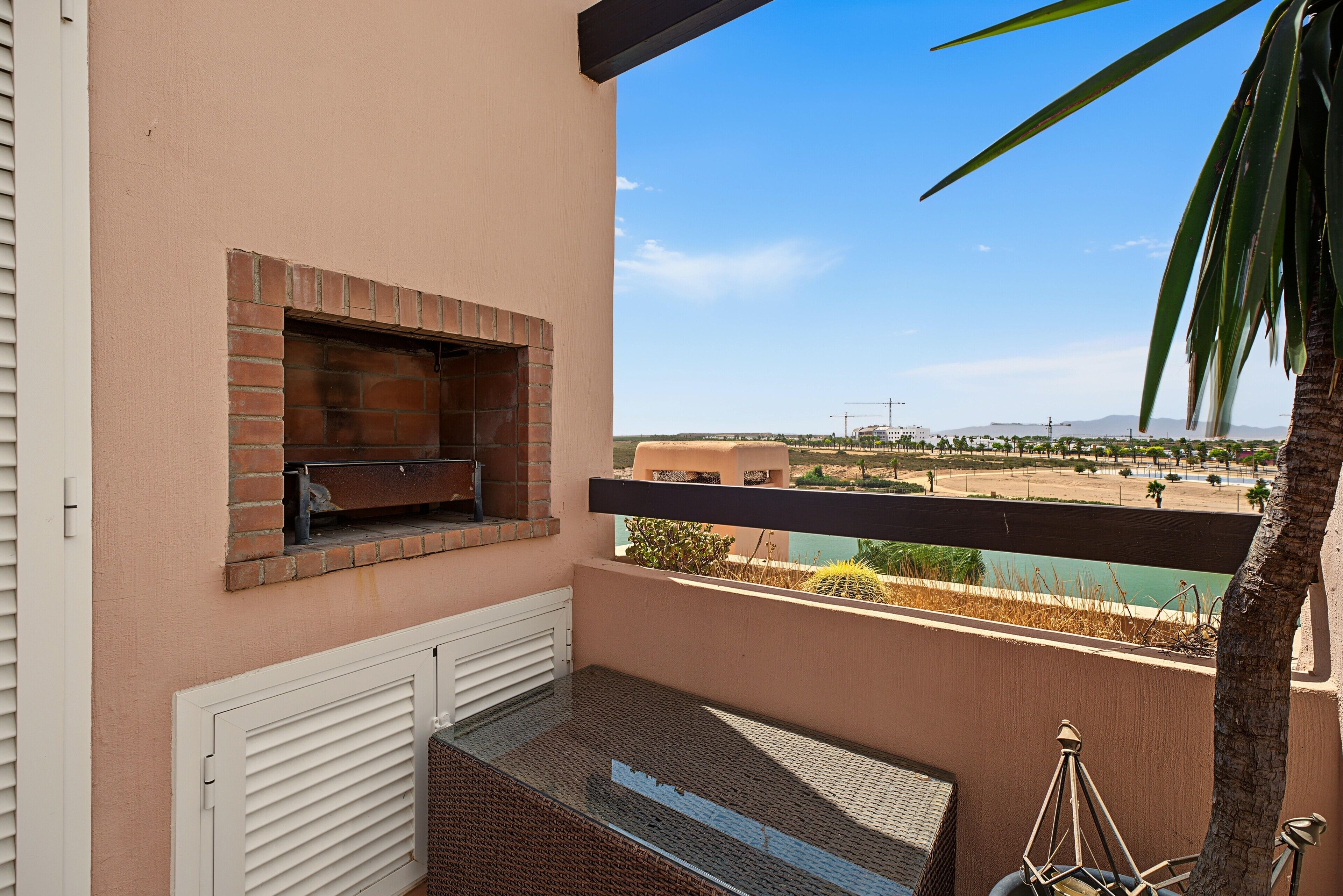 Un balcón con horno de ladrillo, vistas al paisaje desértico y una palmera.