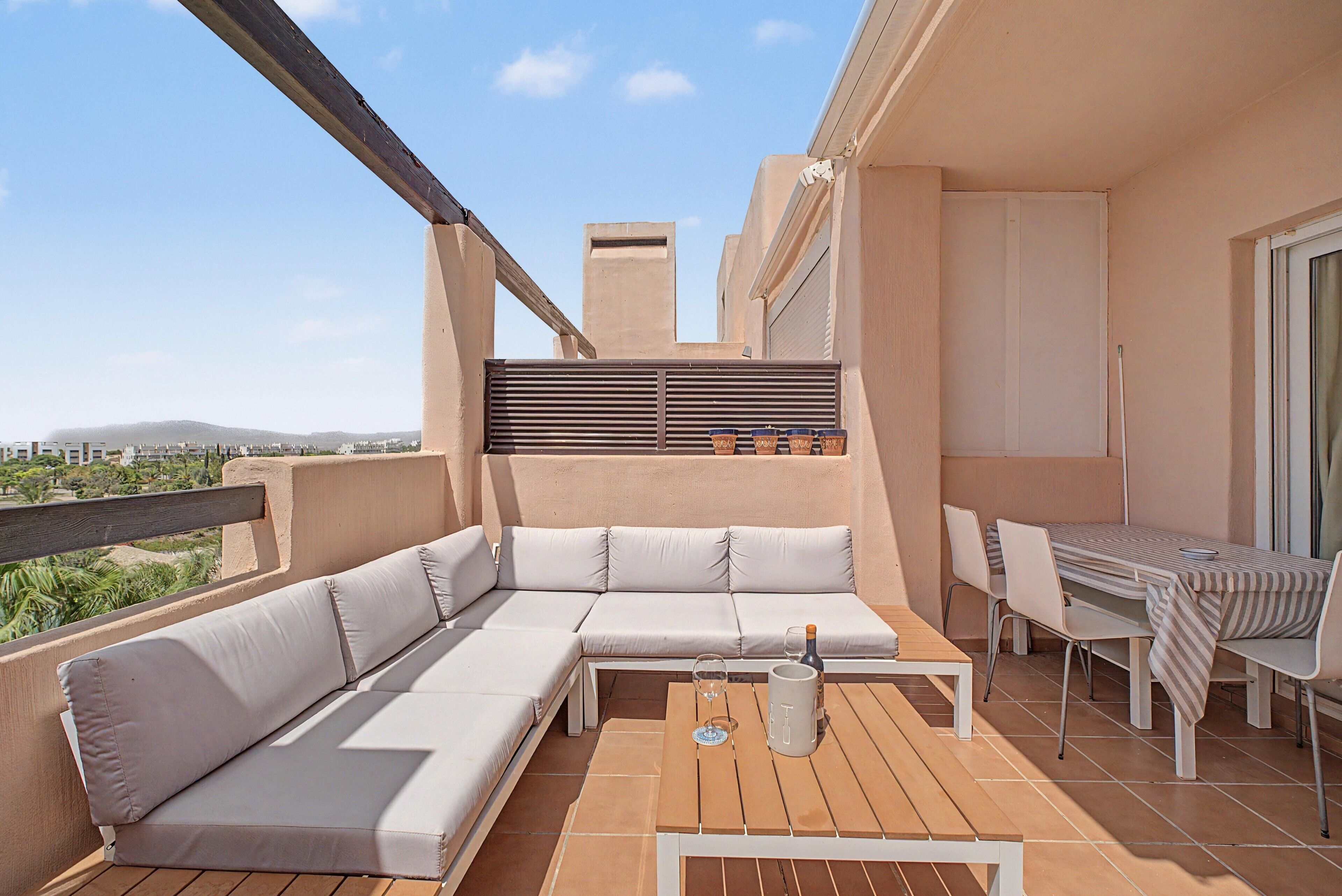 A balcony with a sofa, a table, and chairs, overlooking a cityscape.