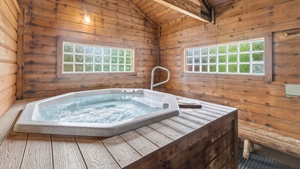 Eine Holzhütte mit Whirlpool, zwei Fenstern mit Dekorglas und einer Holzbalkendecke.