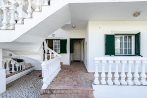 Ein weißes Gebäude mit Treppe, Balkon und einer Tür mit grünen Fensterläden.