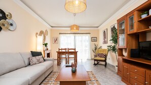 A living room with a sofa, coffee table, dining table, chairs, and a TV stand. - Casa Manuel Vaz Near Tavira (Tavira)