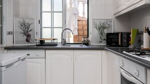 A modern kitchen with white cabinetry, a stainless steel sink, a microwave, and a gas stove. - Casa Manuel Vaz Near Tavira (Tavira)