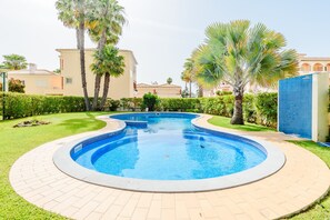Piscina com borda azulejada, rodeada por um caminho de tijolos e vegetação.