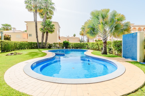 A swimming pool with a tiled edge, surrounded by a brick pathway and greenery. - Vilamoura Garden and Pool Apartment (Loulé)