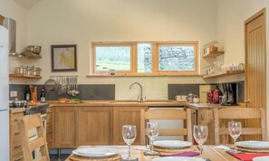 A kitchen with wooden cabinets, a window, and a dining area with chairs and a table set for two. - Maes-Y-Coed -  a self catering cottage that sleeps 8 guests in 4 bedrooms (Dolgellau)