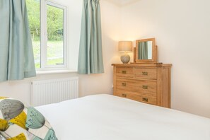 A bedroom with a bed, a wooden dresser with drawers, a mirror, and a window with curtains. - Maes-Y-Coed -  a self catering cottage that sleeps 8 guests in 4 bedrooms (Dolgellau)