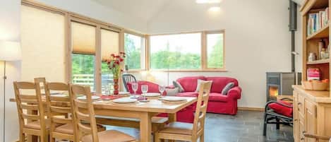 Een eethoek met een houten tafel en stoelen, een rode bank en een open haard.