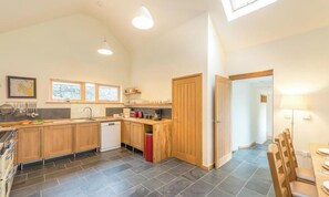 A modern kitchen with wooden cabinets, a dishwasher, and a dining area with a table and chairs. - Maes-Y-Coed -  a self catering cottage that sleeps 8 guests in 4 bedrooms (Dolgellau)