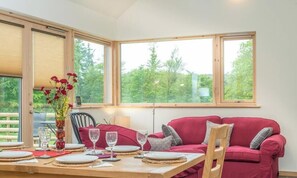 A dining area with a table set for four, a red sofa, and large windows with a view of trees. - Maes-Y-Coed -  a self catering cottage that sleeps 8 guests in 4 bedrooms (Dolgellau)