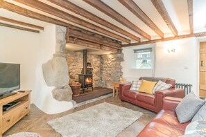 Ein gemütliches Wohnzimmer mit Kamin aus Stein, Holzbalken, einem Ledersofa und einem Fernseher.