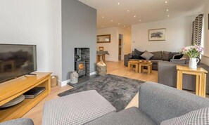Ein modernes Wohnzimmer mit Kamin, grauen Sofas, einem Flachbildfernseher und einem Essbereich.
