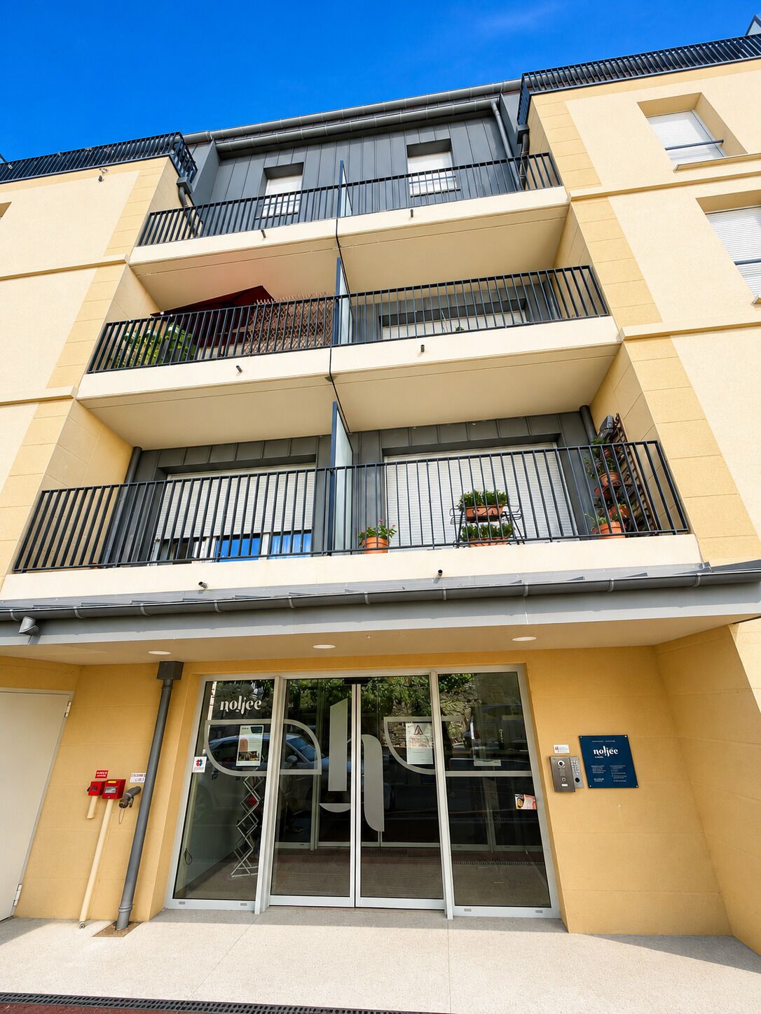 A multi-story building with balconies, a glass entrance, and a sign for 'nojce.'