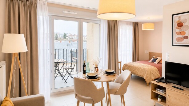 A hotel room with a balcony, a bed, a TV, a desk with a chair, and a dining table.
