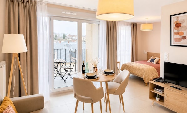 A hotel room with a balcony, a bed, a TV, a desk with a chair, and a dining table. - Zenao Appart'hôtels Limoges (Limoges)