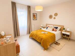 A hotel room with a bed, bedside tables, a desk, a mirror, and a window with curtains.