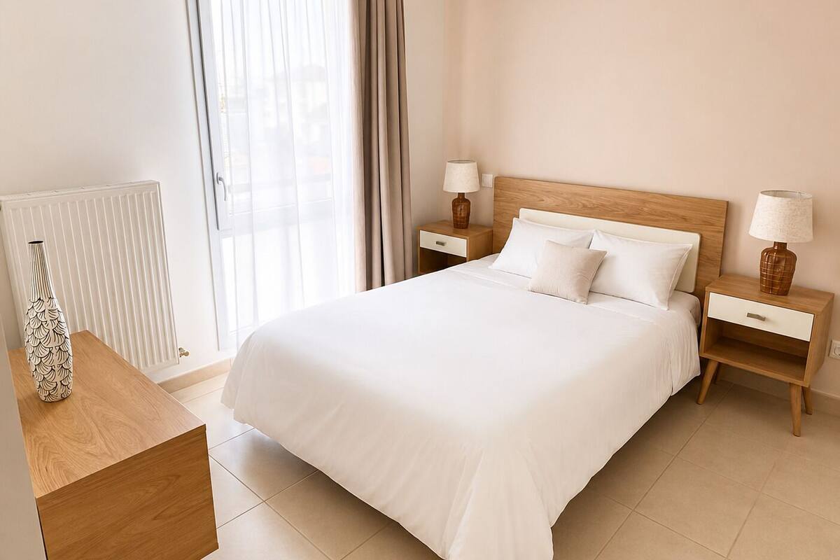 A neatly arranged hotel room with a large bed, two bedside tables with lamps, a radiator, and a window with curtains.
