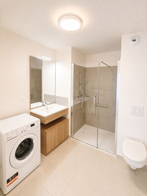 A modern bathroom with a washing machine, a glass-enclosed shower, and a toilet.
