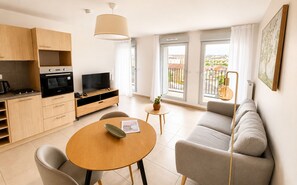 A modern living room with a sofa, a TV, a dining table, and a kitchen area with cabinets and a stove.