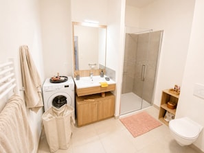 Ein modernes Badezimmer mit Waschmaschine, Waschbecken, Spiegel, Dusche und Toilette.