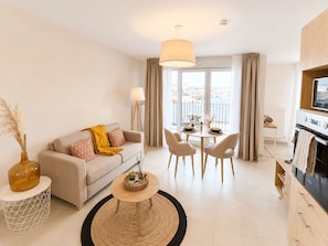 Een modern appartement met een bank, eettafel, stoelen, een keukenhoek en een groot raam met uitzicht.