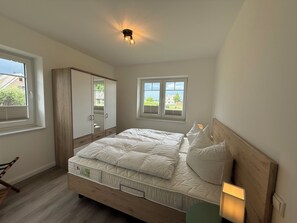 Ein Schlafzimmer mit Bett, Schrank, Fenster und Deckenleuchte.