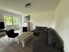 Ein Wohnzimmer mit einer Couch, einem Couchtisch, einem Fernseher und einem Fenster mit Jalousien.