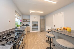 Eine moderne Küche mit Gasherd, Mikrowelle und Kühlschrank. Es gibt Barhocker und eine Frühstückstasse mit Orangensaft.