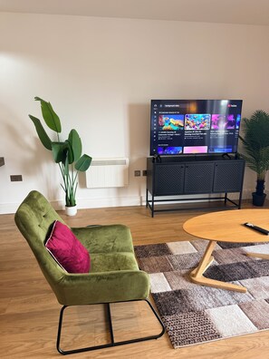 A living room with a green armchair, a television displaying YouTube content, a potted plant, and a wooden coffee table.