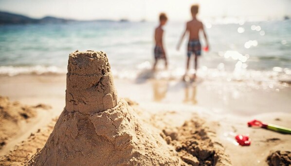 En strandscene med et sandslot i forgrunden og to børn i baggrunden.