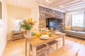 Een eetruimte met een houten tafel, stoelen, een bloemenvaas en een stenen openhaard.