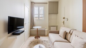 Ein gemütlicher Wohnbereich mit Flachbildfernseher, einem kleinen runden Tisch, einer Couch und einem Fenster mit Vorhängen.